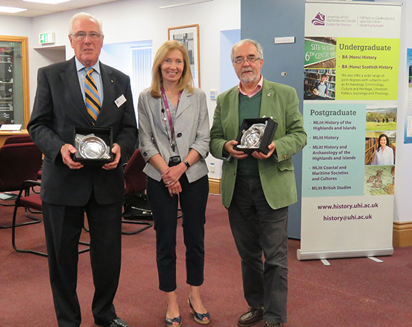 Three people posing, two of them holding awards