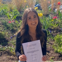 Lauren Geddes sitting on a wall with her completed dissertation