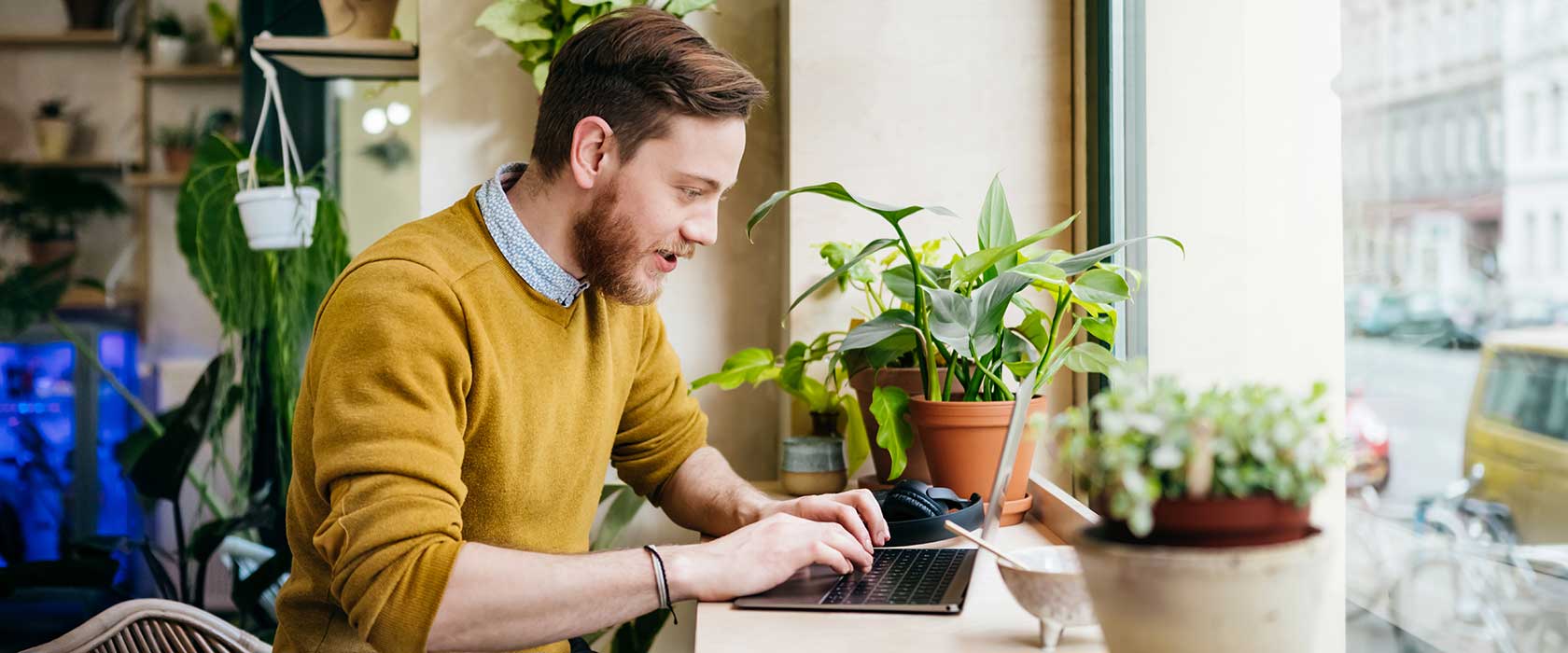 A young person sitting at a laptop in a cafe setting