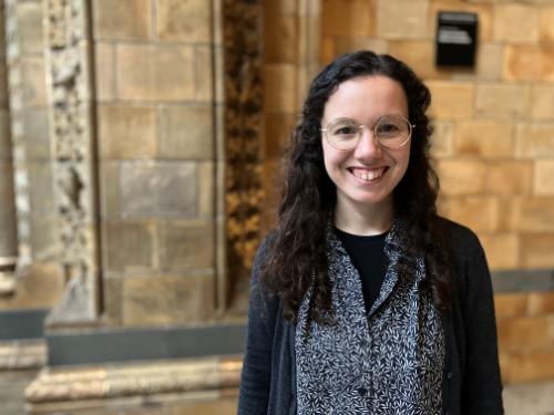 Woman with dark hair and glasses smiling at the camera, standing in front of a sandstone wall Woman with dark hair and glasses smiling at the camera, standing in front of a sandstone wall