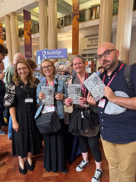 Group of eight people holding books, standing in front of a banner showing the logo for Routledge publishers. Group of eight people holding books, standing in front of a banner showing the logo for Routledge publishers.