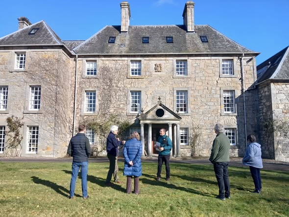 Group of people standing in front of a large stone country house.