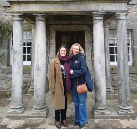 Two women standing in front of a portico with a colonnade.