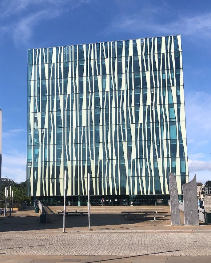 A glass-fronted, cube-shaped building in shades of blue and white, depicted against the blue sky