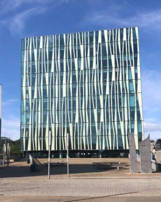 A glass-fronted, cube-shaped building in shades of white and blue, depicted against the blue sky