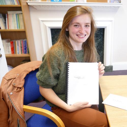 Woman sitting by a table smiling and holding an A4 booklet