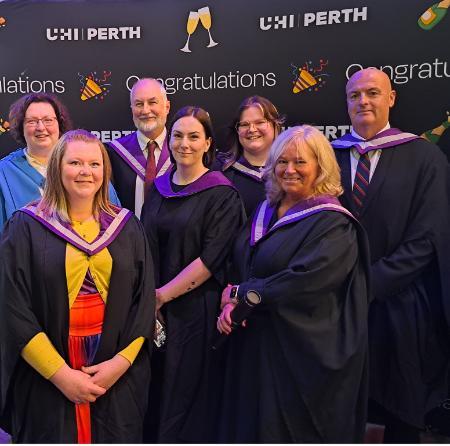 Group of people wearing formal wear and graduations gowns and hoods. Behind them, a backdrop shows repeated texts of UHI Perth and Congratulations, with emojis of champagne flutes and confetti cones Group of people wearing formal wear and graduations gowns and hoods. Behind them, a backdrop shows repeated texts of UHI Perth and Congratulations, with emojis of champagne flutes and confetti cones