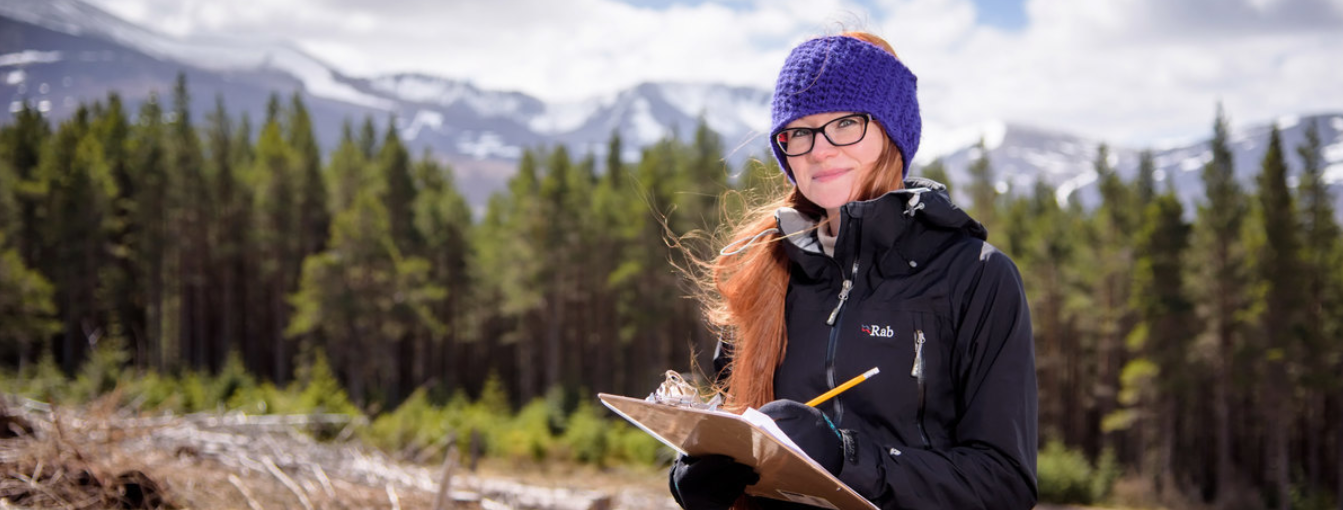 Student outdoors taking notes, snowy mountains in background